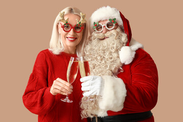 Happy Santa Claus and beautiful mature woman in Christmas glasses with glasses of champagne on brown background