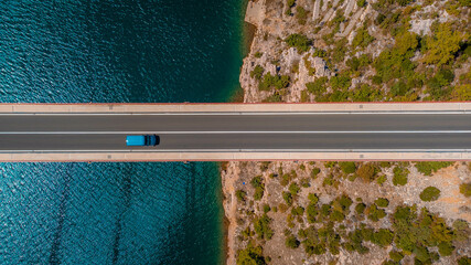 Top down view blue car driving over the bridge over the sea. Background and icon of travel, car journey to discover a country.