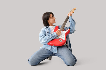Cool young woman playing electric guitar on grey background
