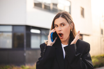 Happy blonde woman talking mobile phone look happy, smiling, open mouth. Business smiling female using mobile phone calling talk. Wow win girl wear black jacket.