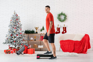 Young happy man training with aerobic stepper in living room decorated for Christmas