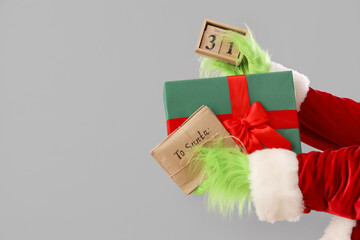 Green hairy hands of creature in costume with Christmas gift box, cube calendar and letters to Santa on grey background