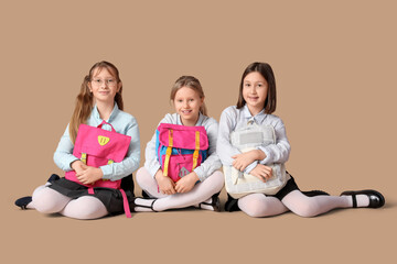 Cute girls in school uniform sitting with backpacks on beige background