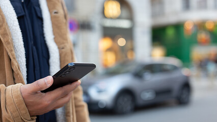 Man using smartphone app for electric car rental service in city