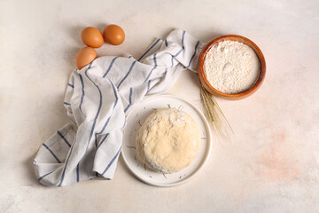 Plate with fresh raw dough, eggs, wheat and bowl of flour on white background
