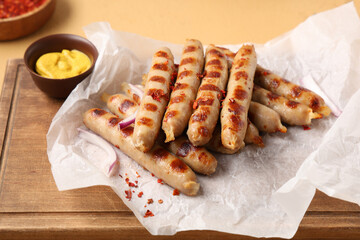 Wooden board with tasty grilled sausages and bowl of mustard on beige background