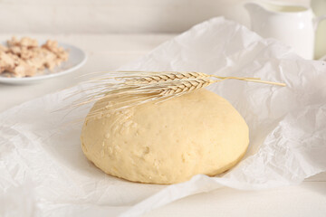 Baking paper with fresh raw dough and wheat on white background