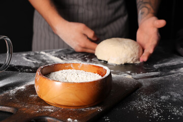 Man with fresh dough and flour on table against black background