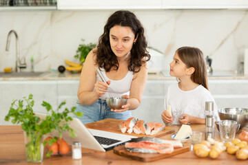 Mom and daughter are preparing festive salmon dish for family dinner. While cooking, mom peeks at...