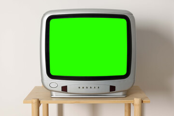 Retro Tv set with green screen on wooden table near white wall. Chroma key