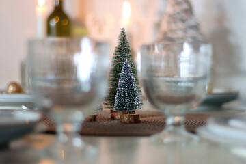 Table set for Christmas meal with plates, glasses, holiday decorations, lit candles and wine. Selective focus.