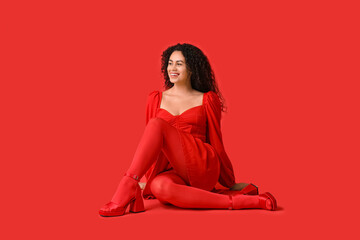 Beautiful young African-American woman in stylish red tights sitting on color background