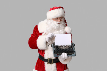 Santa Claus with vintage typewriter on grey background