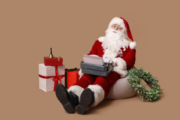 Santa Claus with vintage typewriter sitting on beanbag chair against brown background