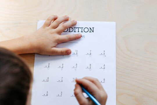 Schoolboy fully engaged in solving addition exercises, practicing math skills at home or in class, writing numbers, calculating sums, and counting for correct answers - Powered by Adobe