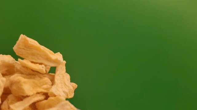 Rotating portion of dried pineapple on a green background.