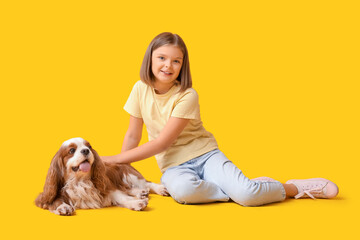 Cute little girl with King Charles spaniel dog sitting on yellow background