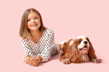 Cute little girl with King Charles spaniel dog lying on pink background