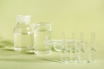 Medical ampules with laboratory glassware and petri dish on green background