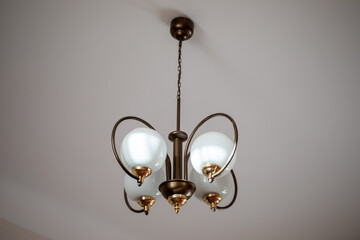 Antique bronze chandelier with round white glass plafonds weighs on chain under ceiling