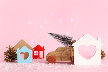Toy wooden car with small Christmas tree, houses and pine cones on pink background