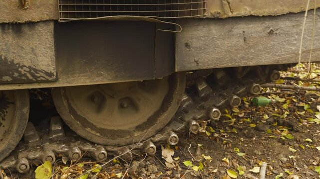 Close-up of muddy tank wheels and tracks, partially covered in dry leaves and twigs. The wheels show signs of use with mud caked on the rims	
