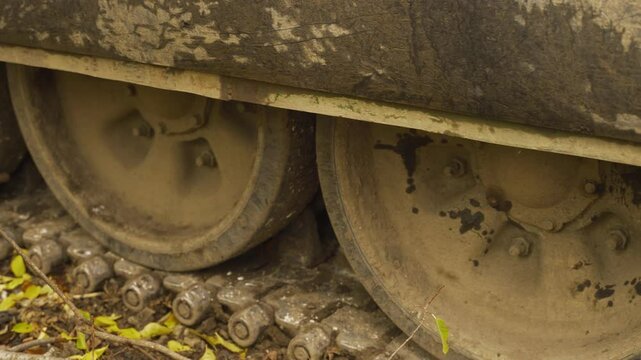Close-up of muddy tank wheels and tracks, partially covered in dry leaves and twigs. The wheels show signs of use with mud caked on the rims	
