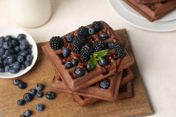 Wooden board of sweet chocolate Belgian waffles with fresh blueberries and blackberries on white background