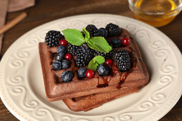 Plate of sweet chocolate Belgian waffles with fresh berries and bowl of honey on wooden background