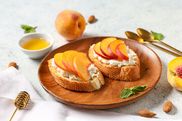 Wooden plate of peach bruschetta with ricotta, almond nuts and bowl of honey on white background