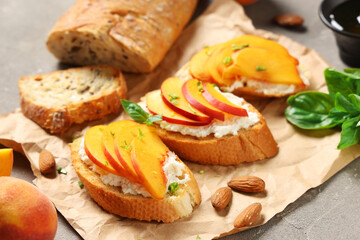 Baking paper of peach bruschetta with ricotta, basil and almond nuts on grey background, closeup