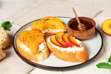 Plate of peach bruschetta with ricotta, mint and bowl of honey on white tile background, closeup
