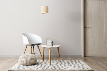 Chair, coffee table with frame, decor and pouf near white wall