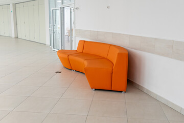 Modern public building interior featuring bright orange modular sofa against white tiled wall....