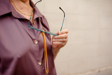 A woman aged 75-80 walks through the street of the city with a phone in her hands. An elderly madam is wearing  white jeans, glasses and a shirt