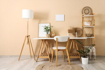 Stylish workplace with shelving unit, lamp and houseplants near beige wall in room