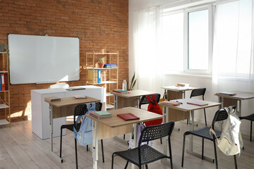 Interior of empty classroom with whiteboard, desks and shelf units