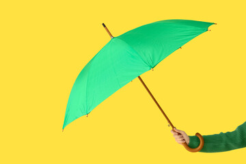 Female hand with green umbrella on yellow background © Pixel-Shot