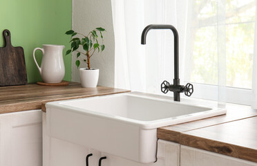 White ceramic sink on wooden counter near green wall in comfortable kitchen