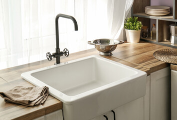 White ceramic sink on wooden counter near window in comfortable kitchen