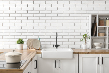 White ceramic sink and shelving unit on wooden counter near white brick wall in kitchen