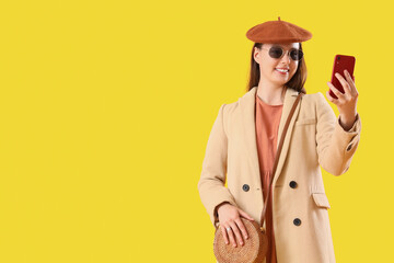 Female tourist in autumn clothes with mobile phone on yellow background