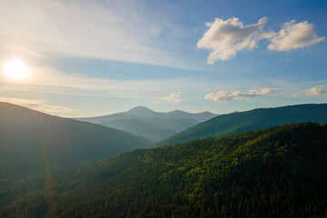 Aerial view of amazing scenery with dark mountain hills covered with forest pine trees at autumn sunrise. Beautiful wild woodland at dawn