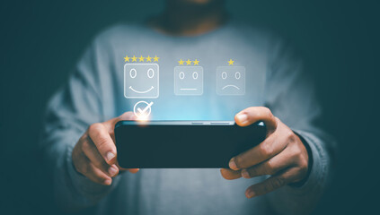Concept of standardization and quality in products and services. Customer satisfaction, Customer uses a smartphone to select smile icon for answer question, Excellent rating, Highest satisfaction,