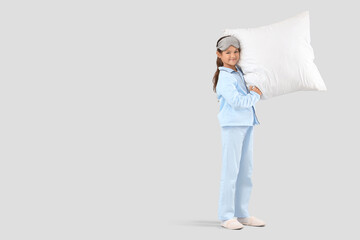 Cute little happy girl in pajamas with sleeping mask and pillow on grey background