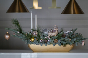 Christmas table composition made of fresh nobilis spruce, white candles, pine branches with glass balls and decorative gold deer. Happy New Year decorations.