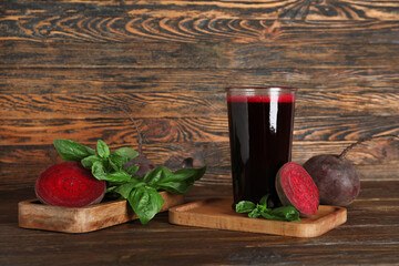 Glass of fresh beet juice with basil and vegetables on wooden background