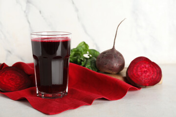 Glass of fresh beet juice with basil and vegetables on white background