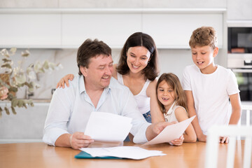 Happy father looking through papers sitting in the kitchen together with wife and children