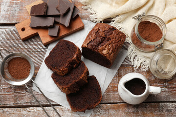 Delicious cut chocolate sponge cake and ingredients on wooden table, flat lay